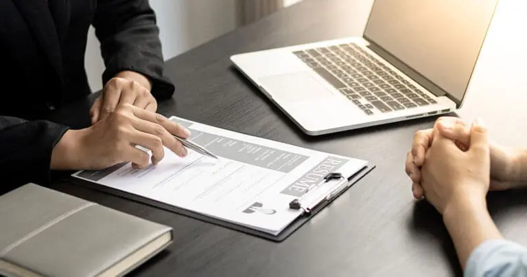 Two people sitting across a desk from each other reviewing a resume on a clipboard together