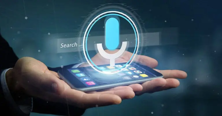 two hands, palms up holding a mobile phone with its screen lit up and a digital graphic of a blue microphone symbol hovering above the phone to symbolize voice search